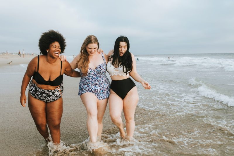 Τρεις χαρούμενες νεαρές με μαγίο και σάκο κολοστομίας στην παραλία